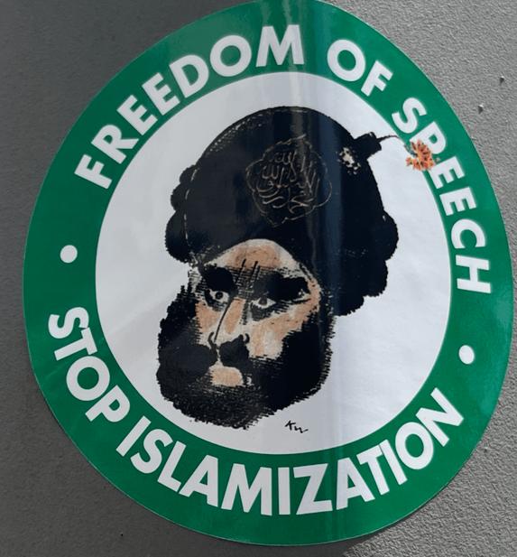 A sticker with a green border surrounding a white circle. It reads "Freedom of speech" on the top, "Stop Islamization" on the bottom. In the mdidle is an illustration of what is supposed to be a muslim man with a bomb in his headwear