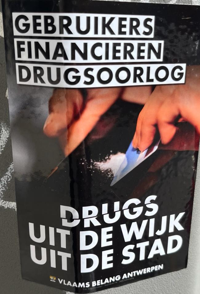 A sticker black/white lettering saying "gebruikers financieren drugsoorlog" and "drugs uit de wijk uit de stad". The background is a picture of hands cutting a line, the logo and name of "Vlaams Belang Antwerpen" rests on the bottom